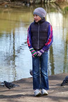a teenager girl standing betwin pigeons birds on the shore of a pond