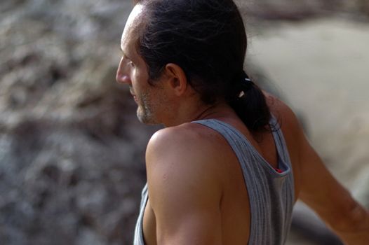 a portrait middle aged man with long hair sideview, outside with rock on background