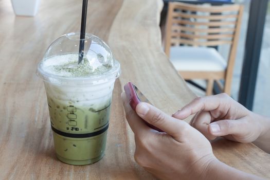 Woman hand holding phone with background of iced green tea, stock photo