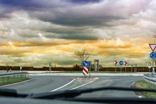 Looking through the windshield of a car on the road. When approaching a Car Roundabouts with dramatic sky in the background.