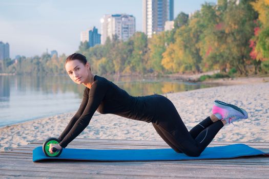 Young pretty fitness woman exercises on pier during morning training workout