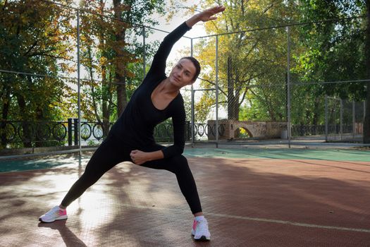 Young pretty fitness woman does stretching exercises during sport training workout on playground outdoor