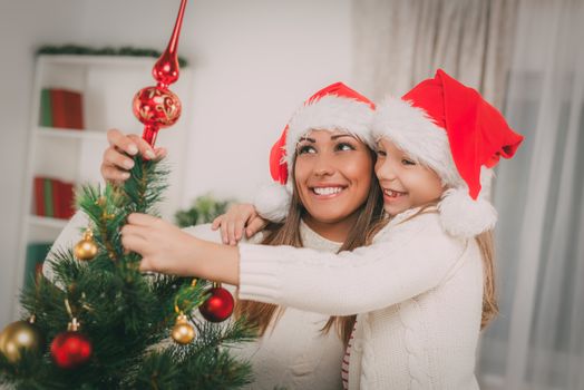 Young mother and her daughter decorating Christmas tree at the home. 