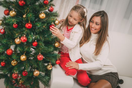 Young mother and her daughter decorating Christmas tree at the home. 