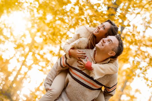 Beautiful young couple enjoying a piggyback in sunny forest in autumn colors. 