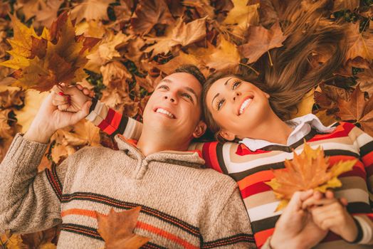 Beautiful smiling couple enjoying in sunny forest in autumn colors. They are lying on the falls leaves.