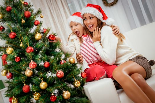 Young mother and her daughter decorating Christmas tree at the home. 