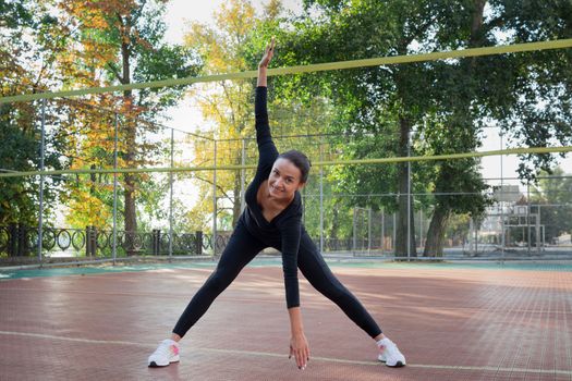 Young pretty fitness woman does stretching exercises during sport training workout on playground outdoor