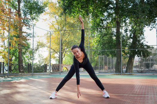 Young pretty fitness woman does stretching exercises during sport training workout on playground outdoor