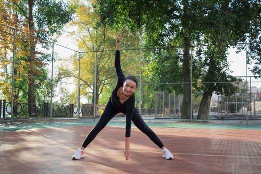 Young pretty fitness woman does stretching exercises during sport training workout on playground outdoor