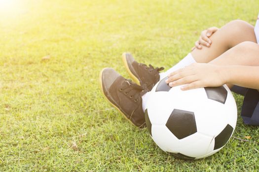 Boy is sitting on green grass with a soccer ball in his hand.Close up1