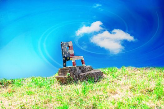 Carved wooden chair on a lawn in Stars and Stripes colors against dramatic sky.