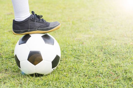 Boy with his foot on top a soccer ball on green grass with sunshine in the evening.Close up1