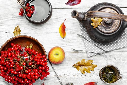 clay kettle with tea with berries on autumn background