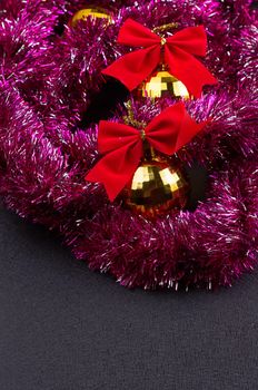 Beautiful Christmas decoration. Gold Christmas balls and bright sparkling golden tinsel with red bows on black background