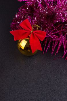 Beautiful Christmas decoration. Gold Christmas balls and bright sparkling golden tinsel with red bows on black background