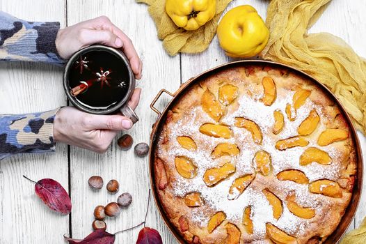 Warm aromatic tea in hand and pie with autumn quince