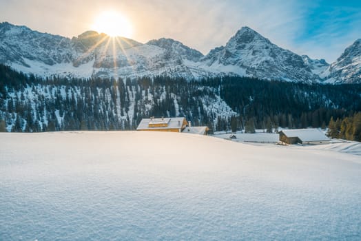Idyllic winter landscape with piles of snow, the Austrian Alps mountains and rustic houses, warmed up by the December sun rays. Image taken in Ehrwald, Austria.