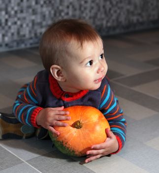 little boy of eight months holding not big orange pumpkin