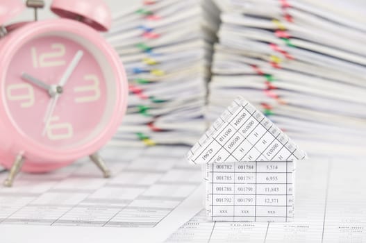 House on finance account have blur old pink alarm clock and pile overload paperwork of report and receipt with colorful paperclip as background.