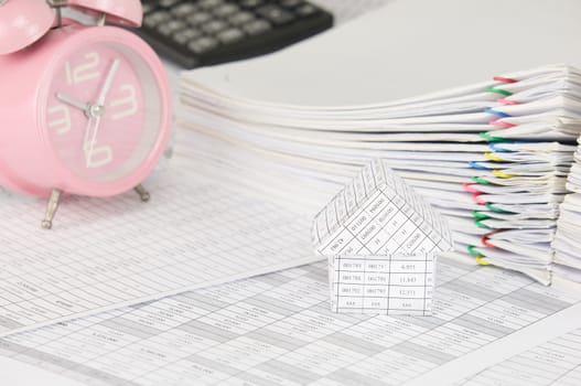 House on finance account have blur old pink alarm clock with calculator and pile overload paperwork of report and receipt with colorful paperclip as background.