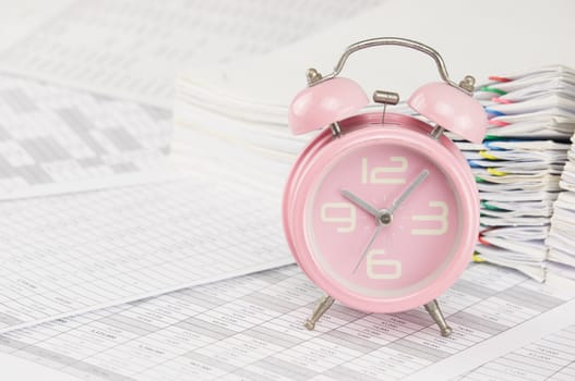 Old pink alarm clock on finance account have blur pile overload paperwork of report and receipt with colorful paperclip as background.