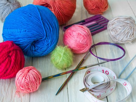 Yarn for hand knitting in different colors, needles, hooks lie on a wooden table