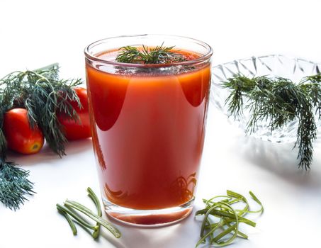 Tomato juice in a tall glass on a white background with herbs and tomatoes
