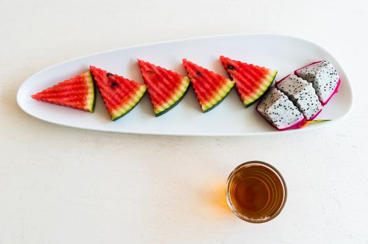 sliced watermelon and dragon fruit on plate with hot tea in the glass, top view