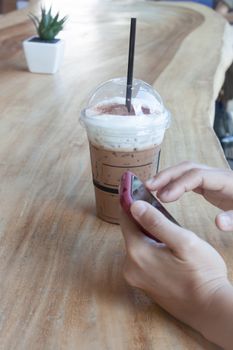 Woman hand holding phone with background of iced coffee, stock photo