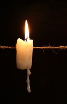 One lighting candle hanging with rope against dark background
