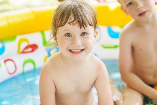 Little children bathe in yellow Inflatable Swimming Paddling Pool outdoors in hot summer day. Kids in Swim Pool