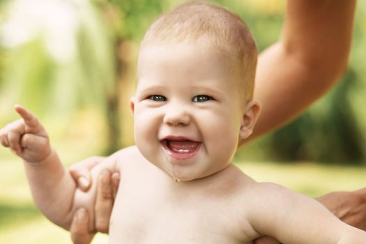 Portrait of a beautiful baby holding the mother's hand against green nature background outdoors