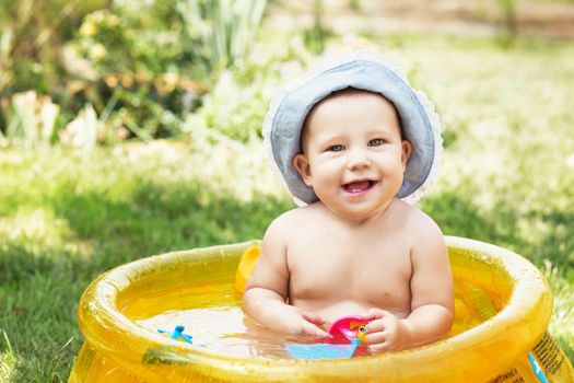 beautiful baby girl in Cotton Panama Cap bathes in yellow Inflatable Swimming Paddling Pool outdoors in hot summer day