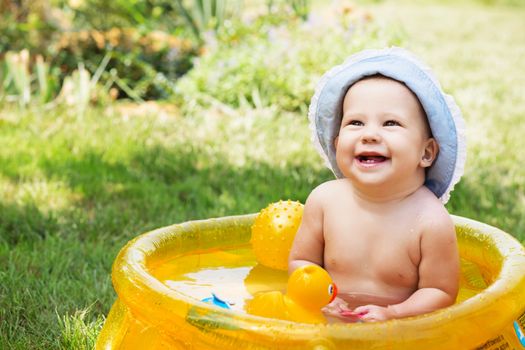 beautiful baby girl in Cotton Panama Cap bathes in yellow Inflatable Swimming Paddling Pool outdoors in hot summer day