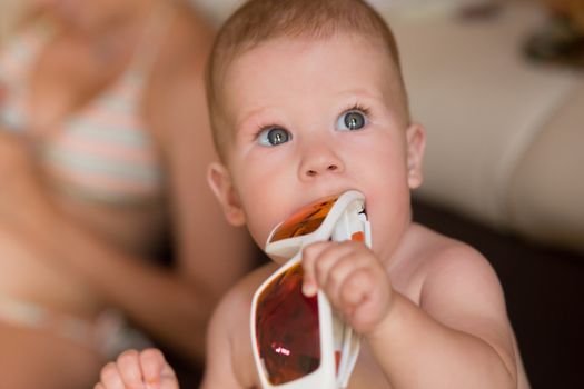 Portrait of a beautiful baby plays with sunglasses. The concept of the eruption of primary teeth in infants