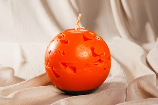 orange candle on textured fabric surface. Souvenir gift candle in the shape of Carved pumpkin. A burning candle. Candle lit. Halloween