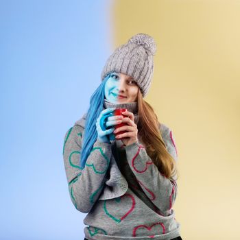 Cute teenage girl wearing gray woolen cap and scarf warming her hands on a cup of hot tea. Frozen girl thaws of hot tea
