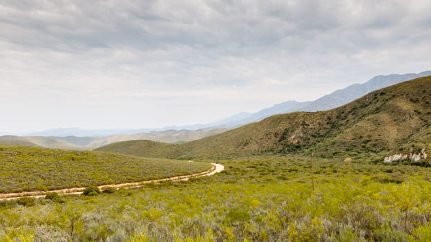 Cloudy day with green valley and the road leading thru the mountains.