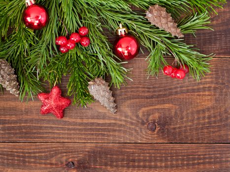 Christmas fir tree with decoration on dark wooden board background. Border art design with Christmas tree, cones and red baubles. Xmas and new year concept. Top view or flat lay with copy space
