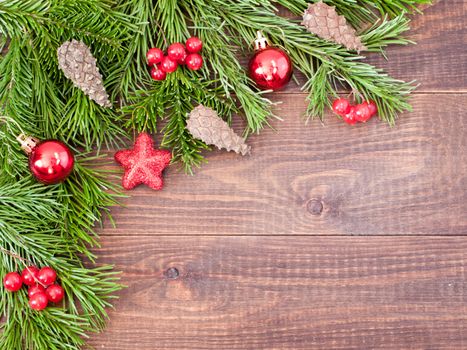 Christmas fir tree with decoration on dark wooden board background. Border art design with Christmas tree, cones and red baubles. Xmas and new year concept. Top view or flat lay with copy space