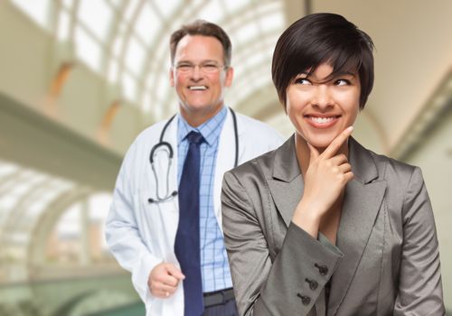 Happy Mixed Race Woman Looking To The Side As Male Doctor Stands Behind Her Inside Hospital.