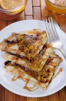 Breakfast pancakes on apples with caramel and chocolate and cup of tea