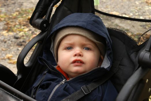 A cute baby boy is all bundled up during his stroll in the colder northern autumn weather.