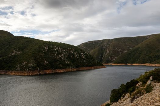 Low water level at the inlet to the Kouga Dam with clouds and valley.