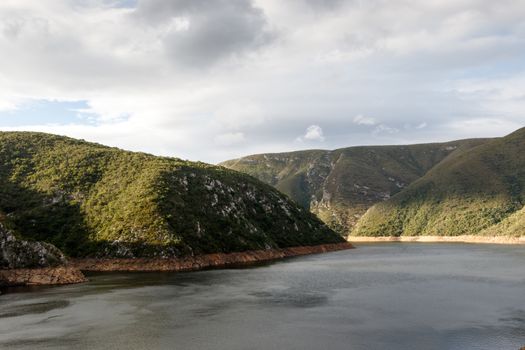 Close up view - Low water level at the inlet to the Kouga Dam with clouds and valley.