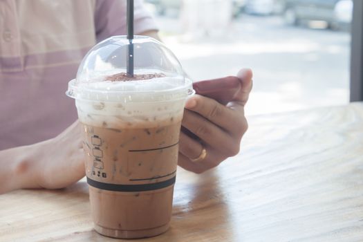 Woman hand holding phone with background of iced coffee, stock photo