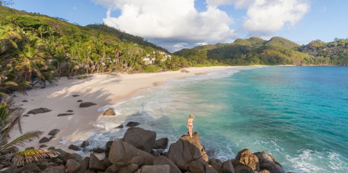 Woman in bikini enjoying beautiful view of Ance Intendance paradice beach from perfect round rocks on Mahe Island, Seychelles. Summer vacations on picture perfect tropical beach concept.