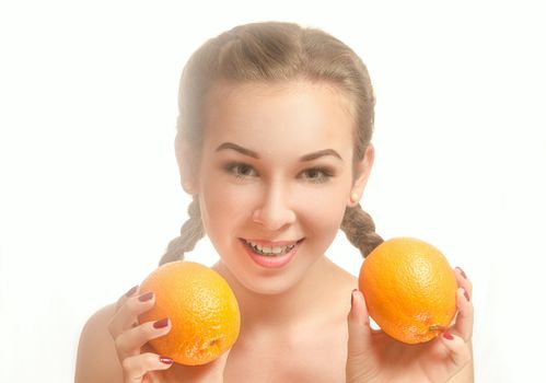 Young pretty girl with two oranges and pigtails is smiling on a white background