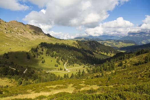 Mountain landscape with valley, trails, green fields and blue sky with clouds